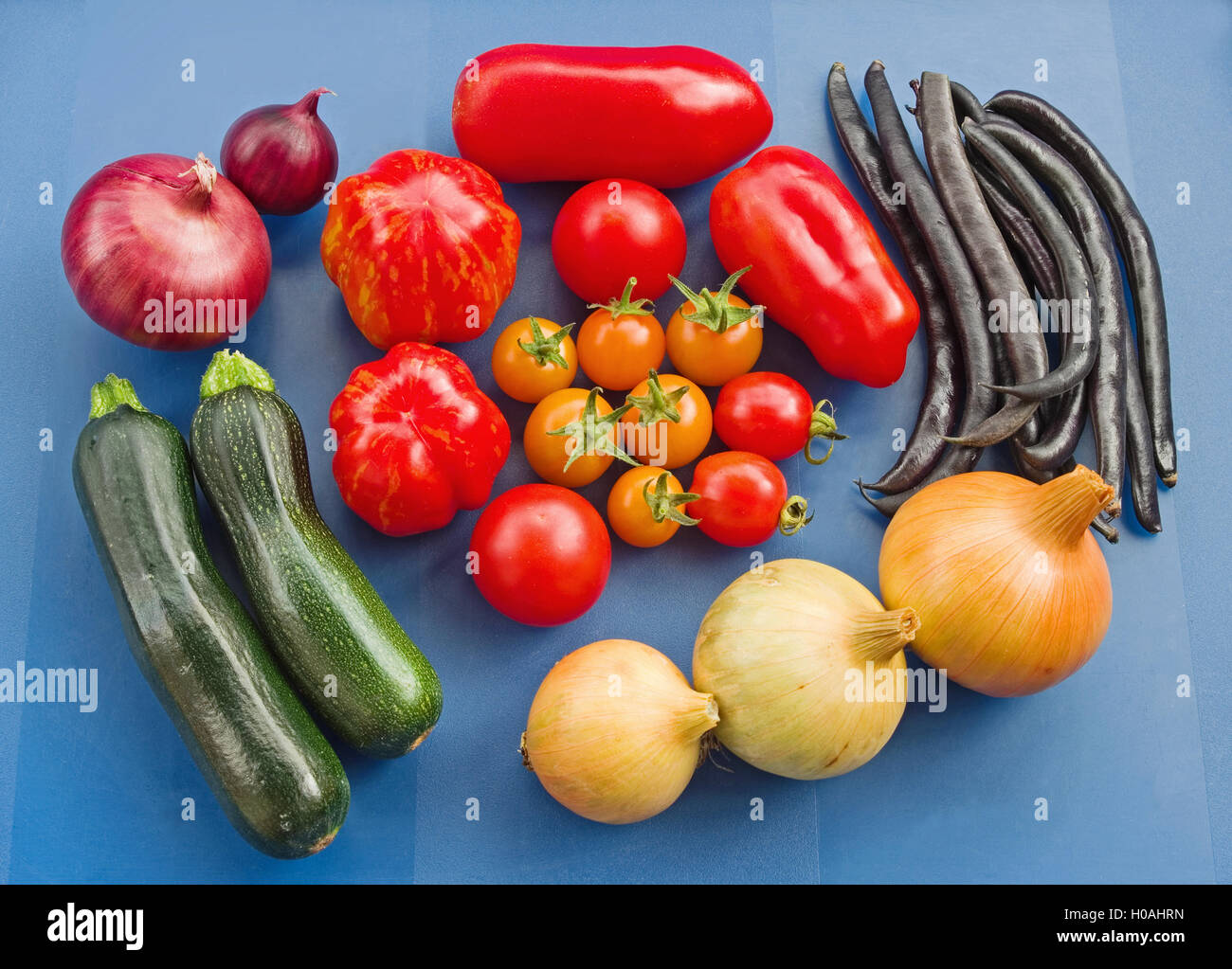 Arrangement d'un assortiment de variétés de tomates fraîchement cueillies, et autres légumes du jardin d'été, sur un fond bleu. Banque D'Images