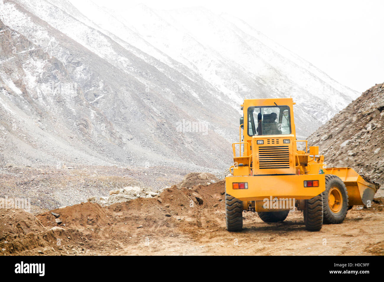 Grand véhicule de la machinerie lourde de labourer le sable et les pierres pour passer au chemin de montagne neige Banque D'Images