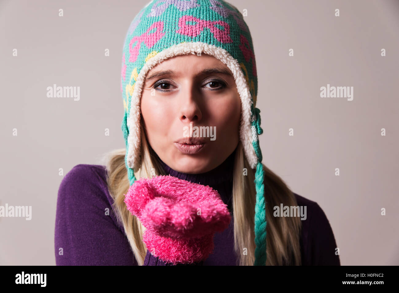 Femme portant un chapeau tricoté et un gant chaud soufflant un baiser Banque D'Images