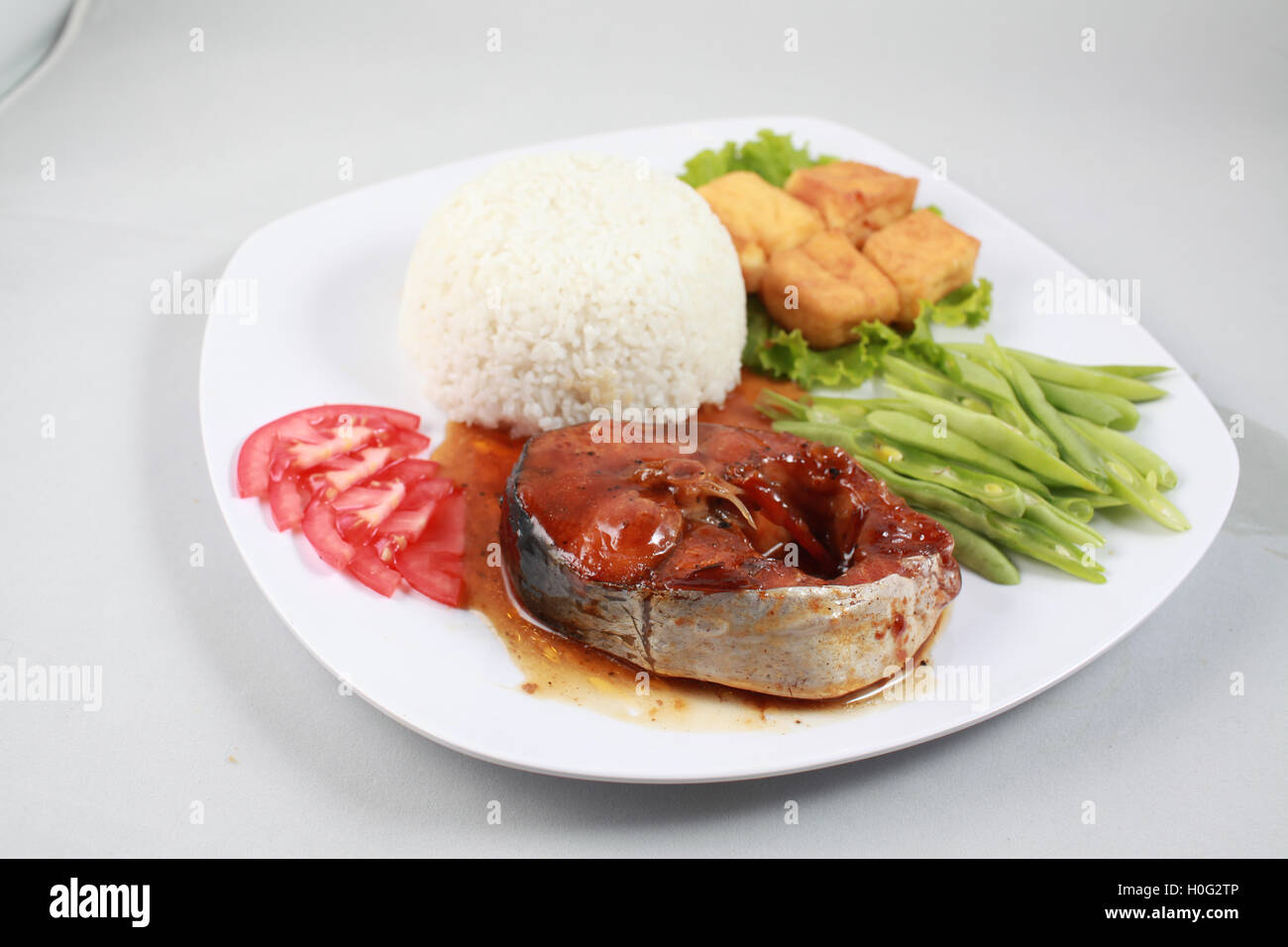 Le riz ordinaire avec longe braisé sur le poisson-chat, du tofu frit et haricots verts cuits sur plaque blanche dans le delta du Mékong Banque D'Images