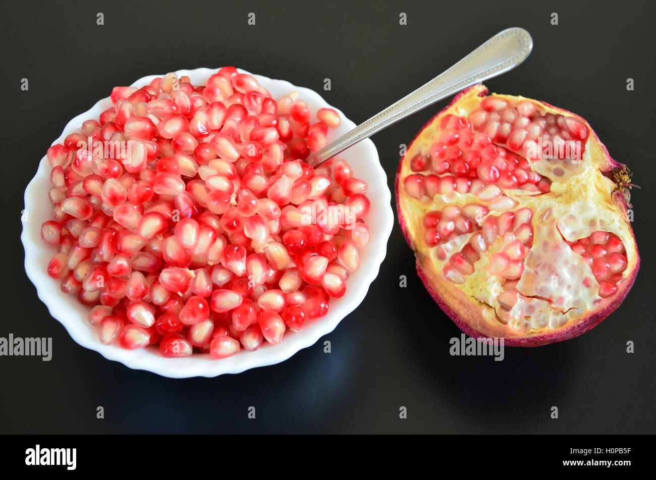 Bowl full of red juicy pomegranate perles avec une cuillère et la moitié de grenade Banque D'Images