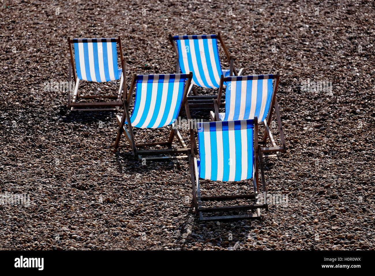 Rayé bleu et blanc 5 chaises vides sur une plage de galets Banque D'Images