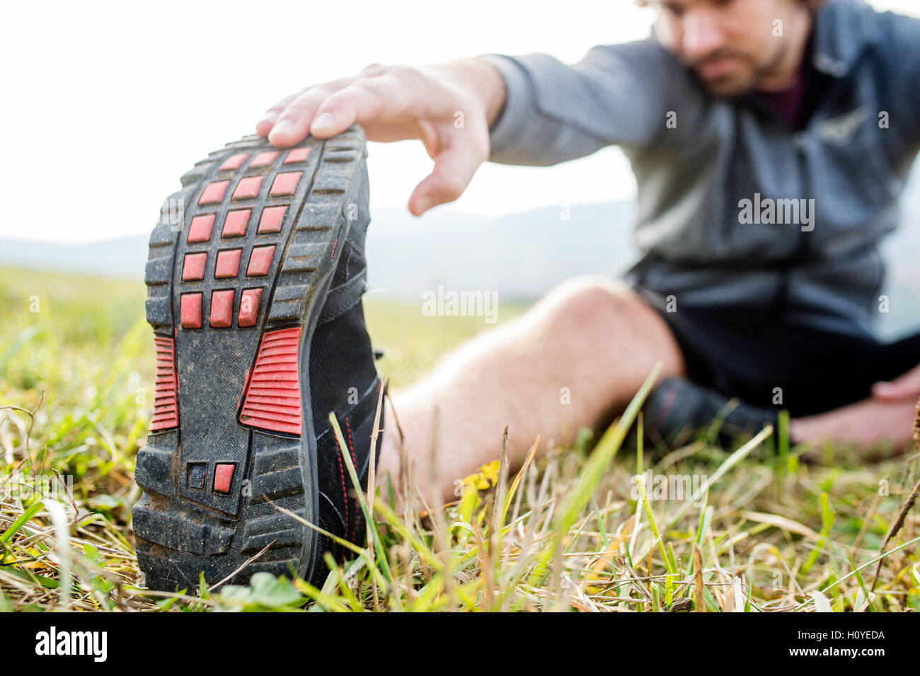 Méconnaissable young runner sitting on grass, stretching leg Banque D'Images