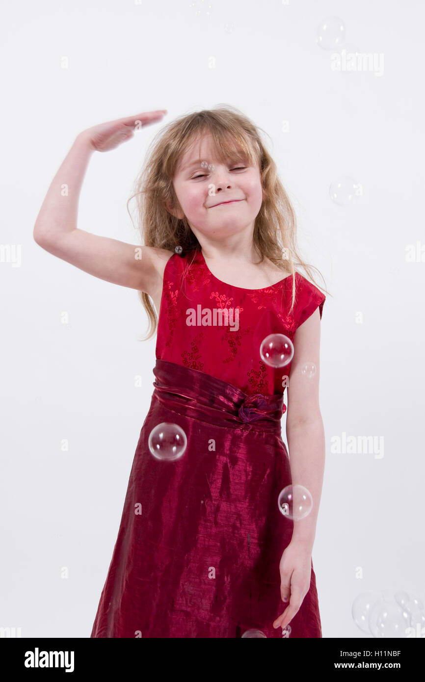 Jeune fille portant robe de soirée rouge brillant pats en riant à sa tête, une bulle pop studio portrait isolated on white Banque D'Images