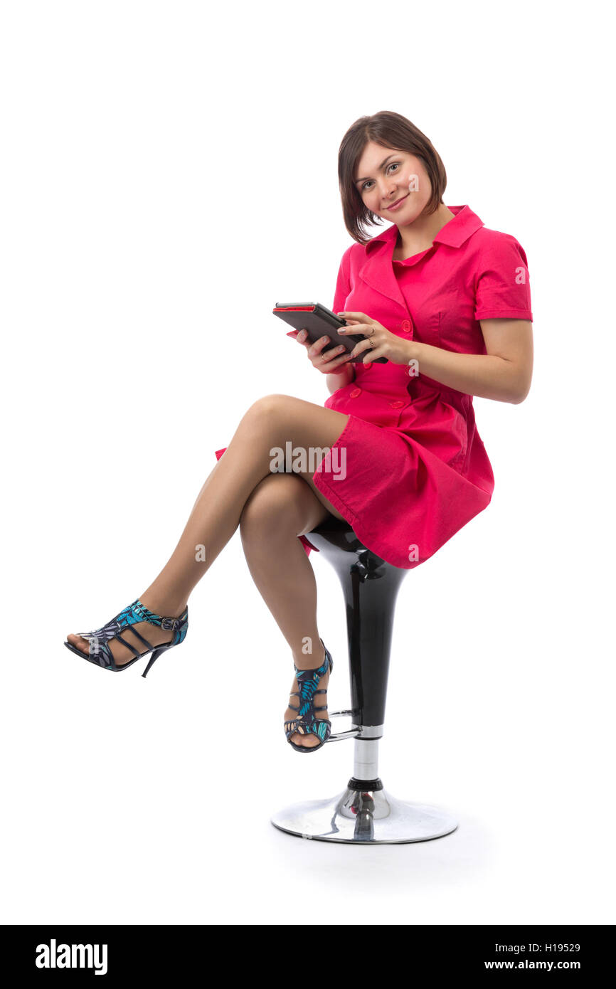 Jeune fille dans une robe rouge avec un Tablet PC dans les mains sur une chaise bar dans le studio. Isoler sur blanc. Banque D'Images