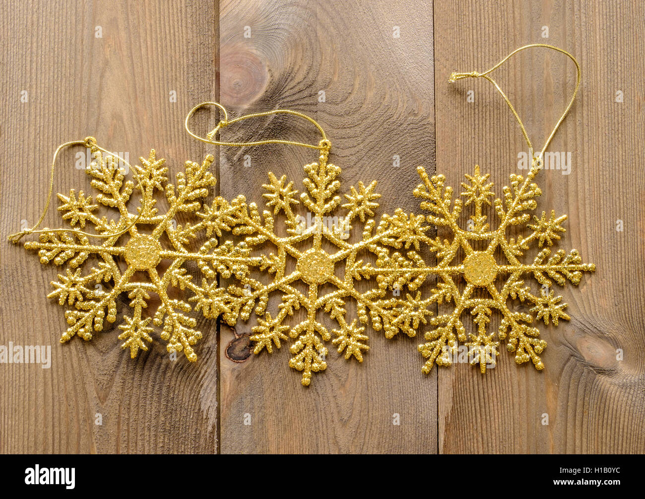 Groupe de trois sparkly glitter gold snowflake Christmas Tree decorations de la poser à plat sur fond de bois Banque D'Images