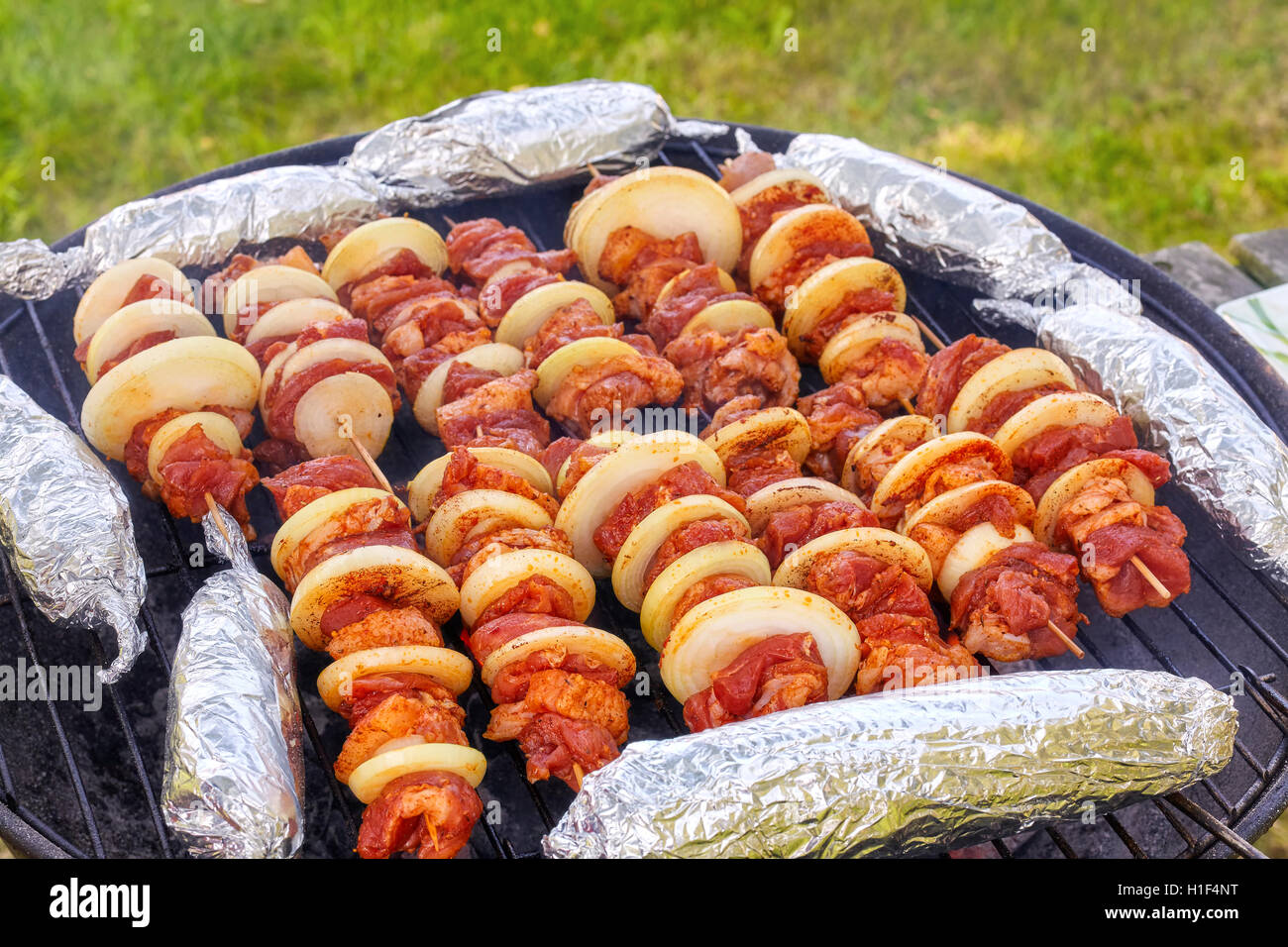 Close up photo de brochettes de viande avec des oignons et des épis de maïs dans de l'aluminium, jardin barbecue, selective focus. Banque D'Images