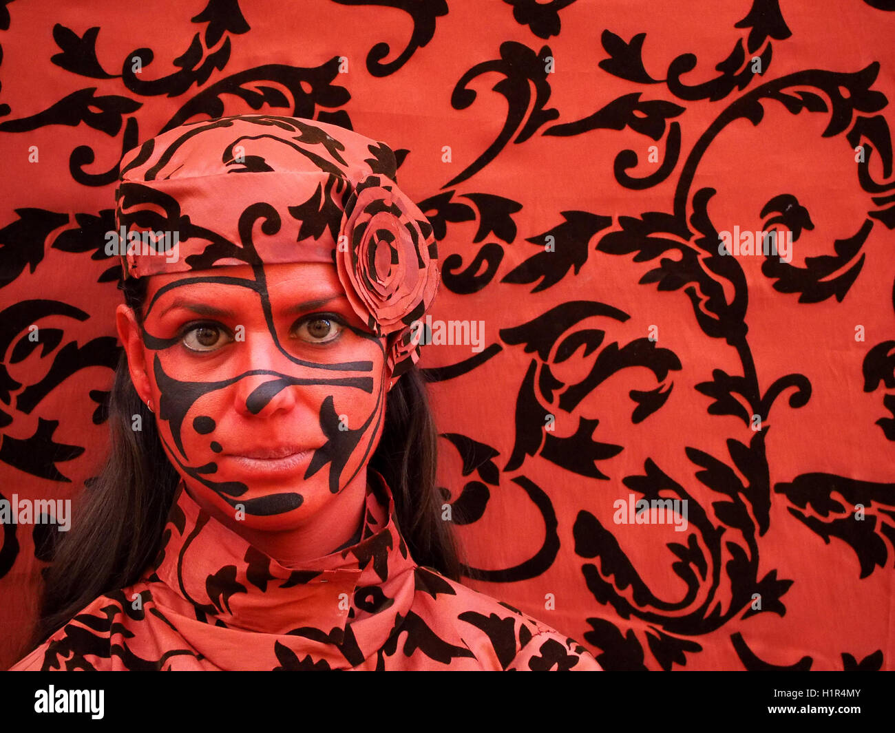 Artiste de performance fixant peintes pour correspondre à motifs noir et rouge profond fond tissu velours immobile comme une statue Banque D'Images