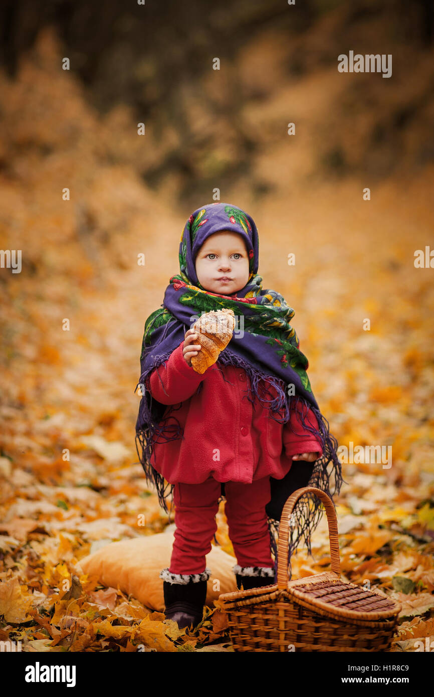 Fille enfant en ukrainien folk foulard sur la tête avec imprimé floral. Manger petit pain dans la forêt d'automne Banque D'Images