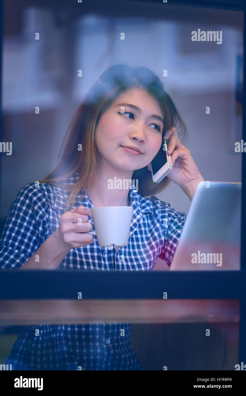 Portrait de l'Asie jolie femme parlant au téléphone tout en restant assis dans un café et profiter du café, du concept des vacances. Banque D'Images
