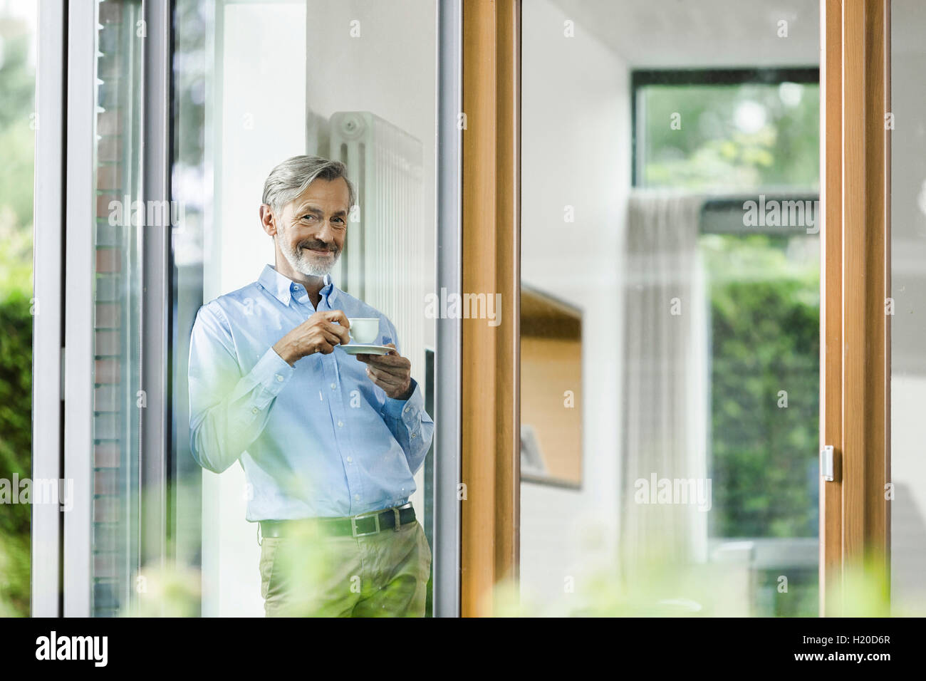 Smiling man avec tasse de café debout dans sa maison à la recherche d'une fenêtre Banque D'Images Smiling man avec tasse de café debout dans sa maison à la recherche d'une fenêtre Banque D'Images