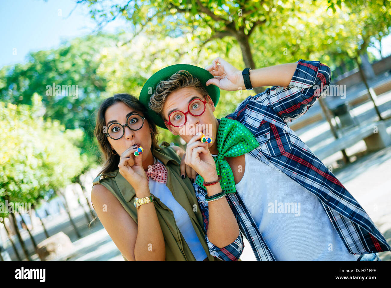 Young couple having fun with party blowers, lunettes et chapeaux de blague Banque D'Images