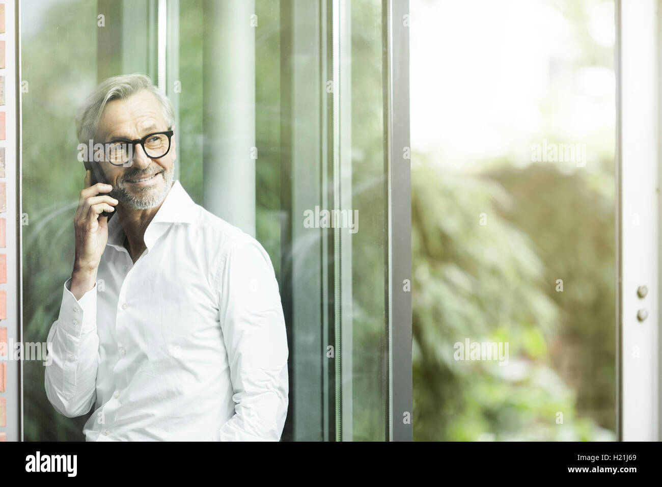 Portrait of smiling man on the phone debout devant sa maison Banque D'Images Portrait of smiling man on the phone debout devant sa maison Banque D'Images