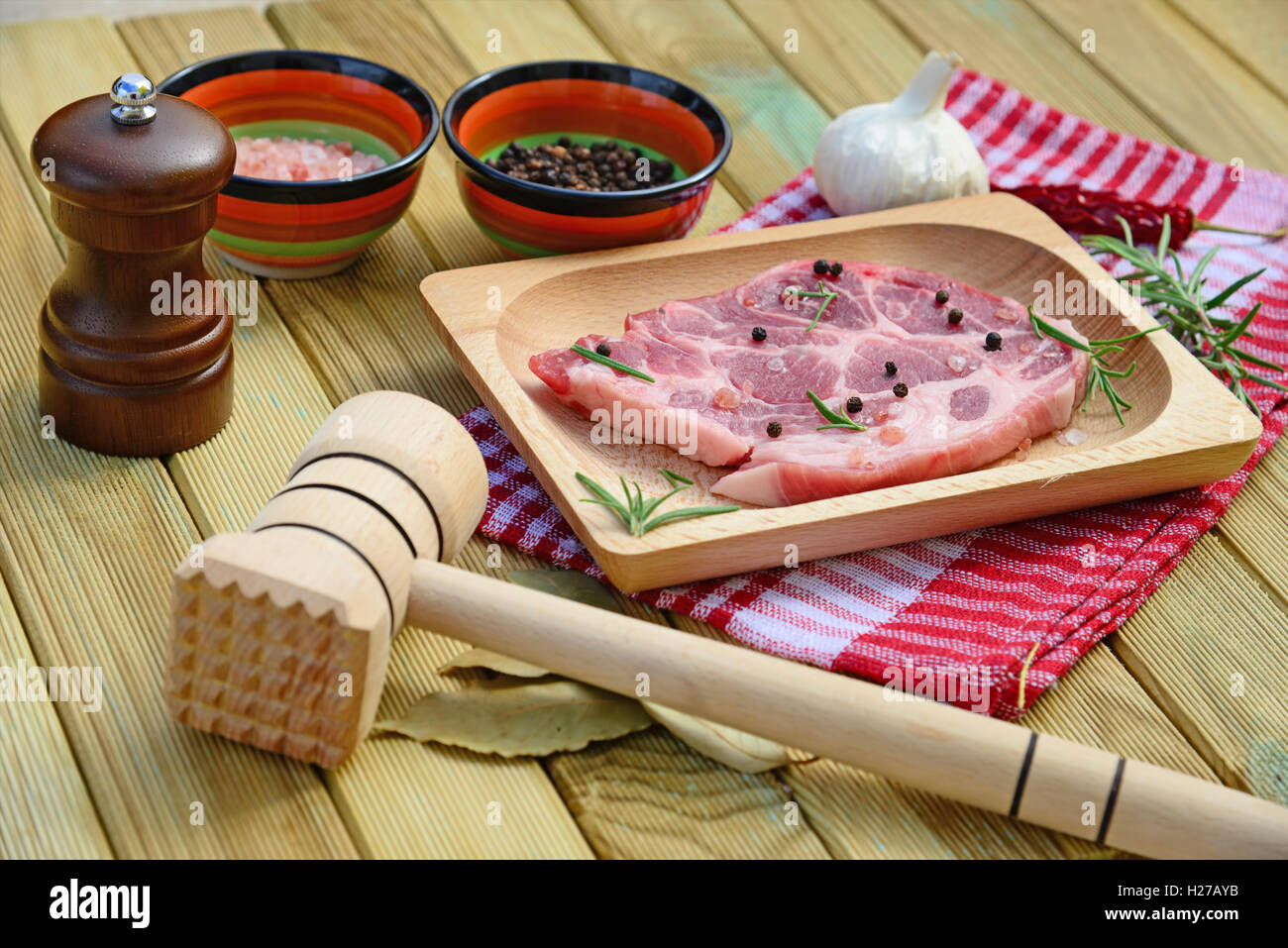 La viande de porc cru sur plaque de bois, moulin à poivre, romarin, épices et un marteau sur fond de bois Banque D'Images