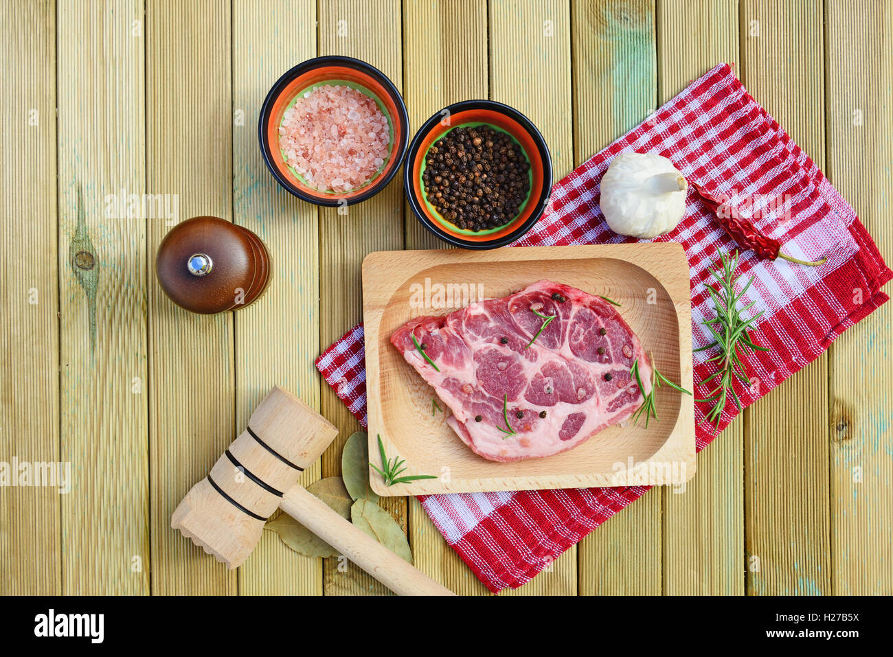 La viande de porc cru sur plaque de bois, moulin à poivre, romarin, épices et un marteau sur fond de bois Banque D'Images