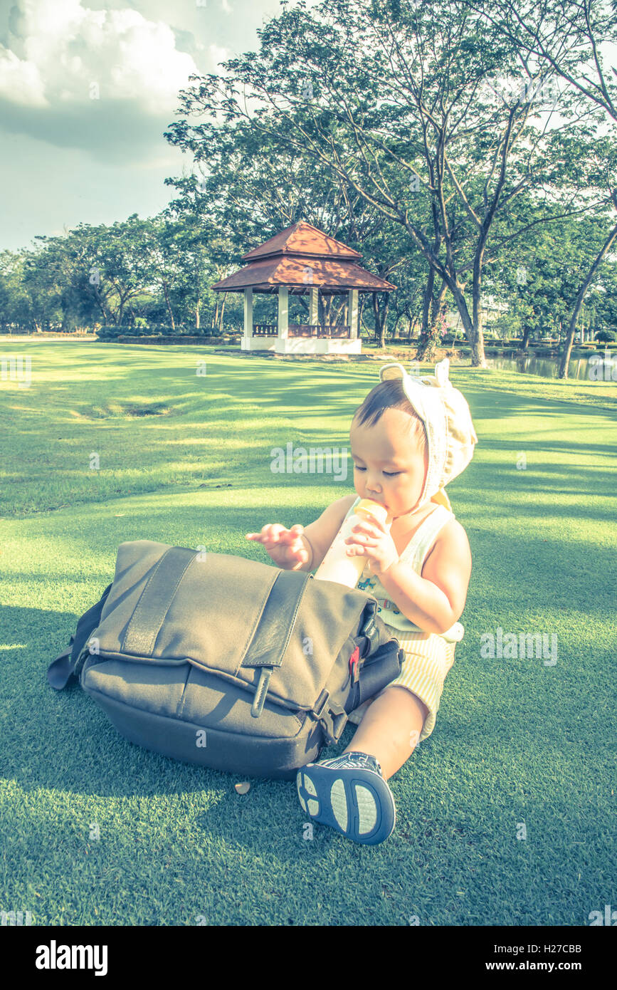 Adorable bébé garçon asiatique boire du lait en bouteille quand pique-nique en famille dans le parc de porte de sortie, l'effet de couleur pastel Banque D'Images