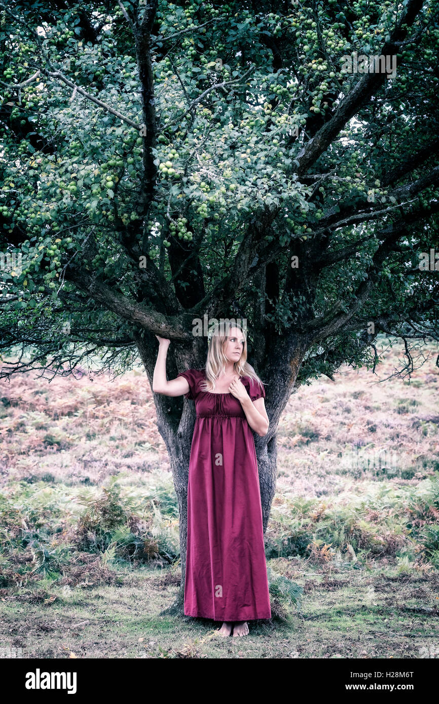 Une femme blonde avec une robe rouge est debout sous un arbre Banque D'Images