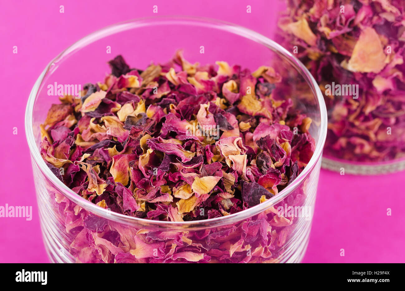 Des pétales de rose dans un bol en verre sur fond rose. Fleurs séchées, utilisées pour des parfums, des cosmétiques, du thé et des bains. Banque D'Images