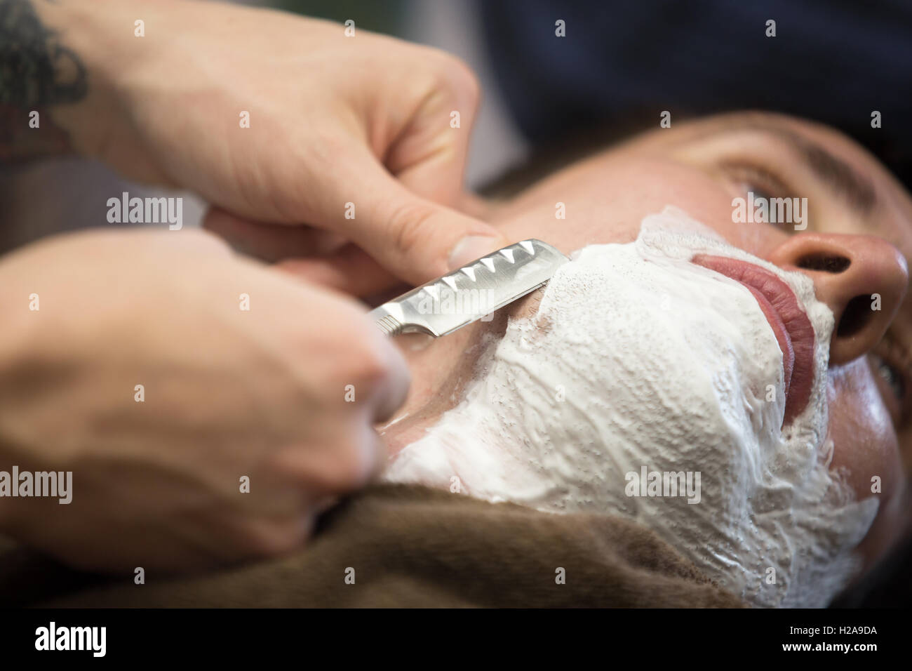 Tourné de l'intérieur de processus de travail moderne dans un salon de barbier. Close-up portrait of beau jeune homme se raser la barbe avec straig Banque D'Images