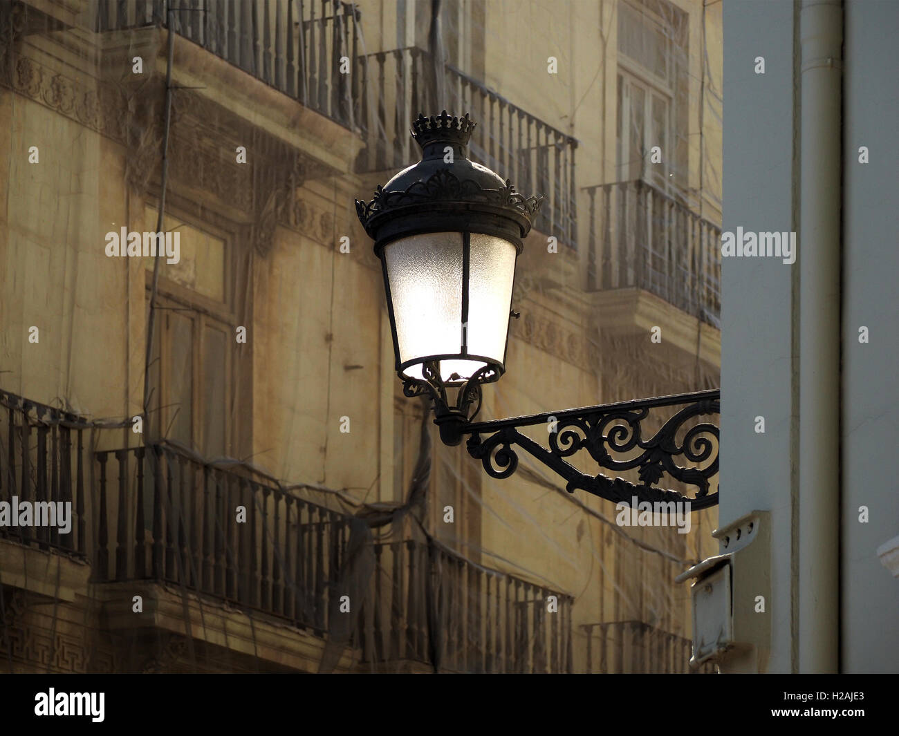 Soleil blanc sur plaque de verre et le support aux éléments en fer forgé se détachant sur la façade de l'immeuble aux balustrades en pierre dans l'ombre tamisée Espagne Banque D'Images