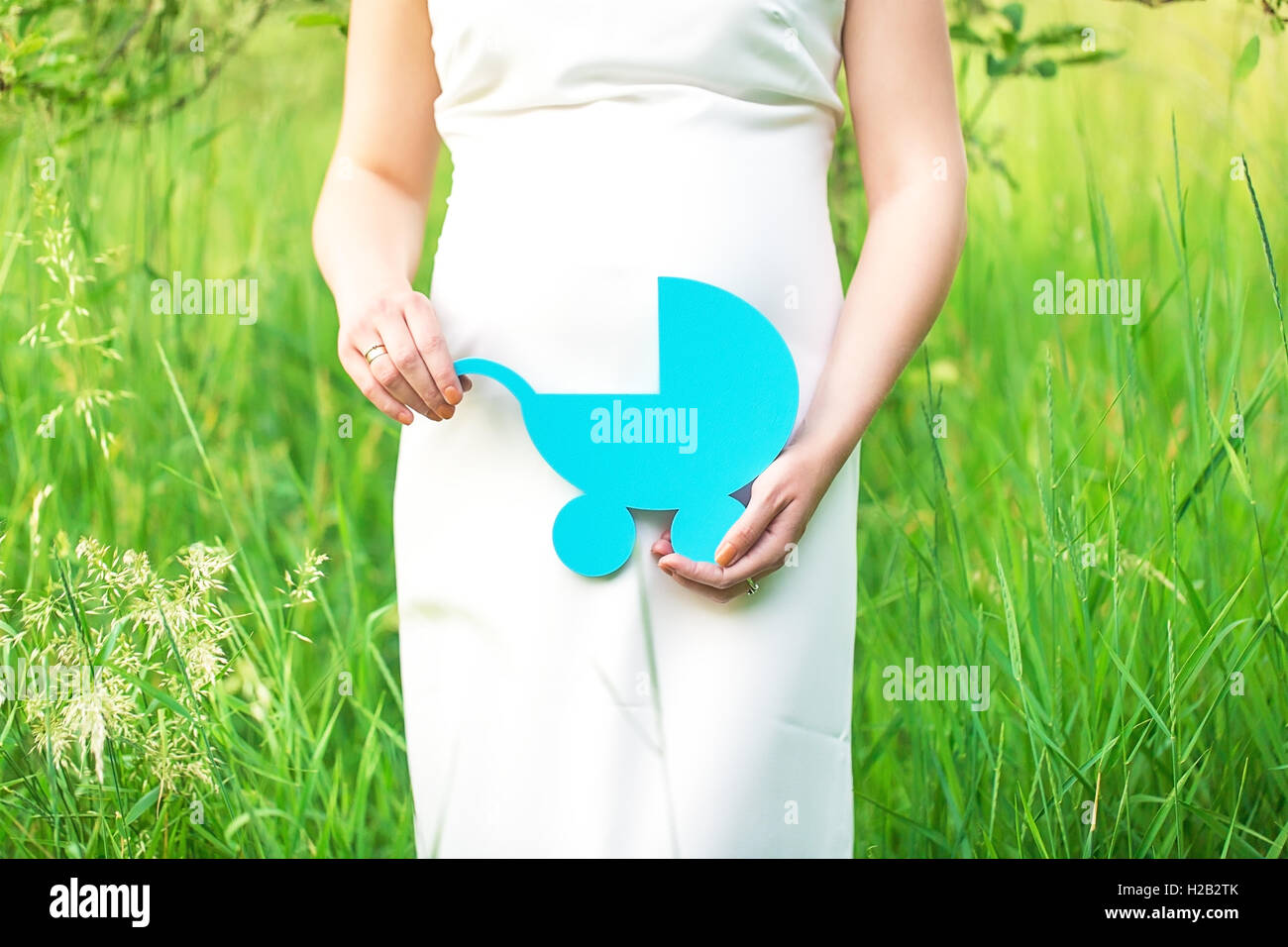 Belle jeune femme enceinte tenant un bébé sur l'abdomen, dans le jardin sur un fond d'herbe Banque D'Images
