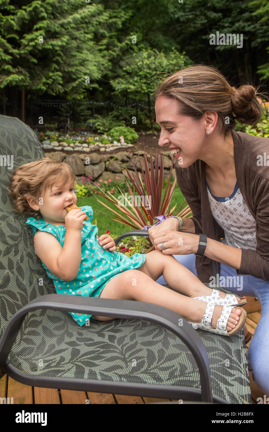 Jeune fille de dix-huit mois, une barre granola manger dehors avec sa mère joyeusement la taquiner, à Issaquah, Washington, USA Banque D'Images