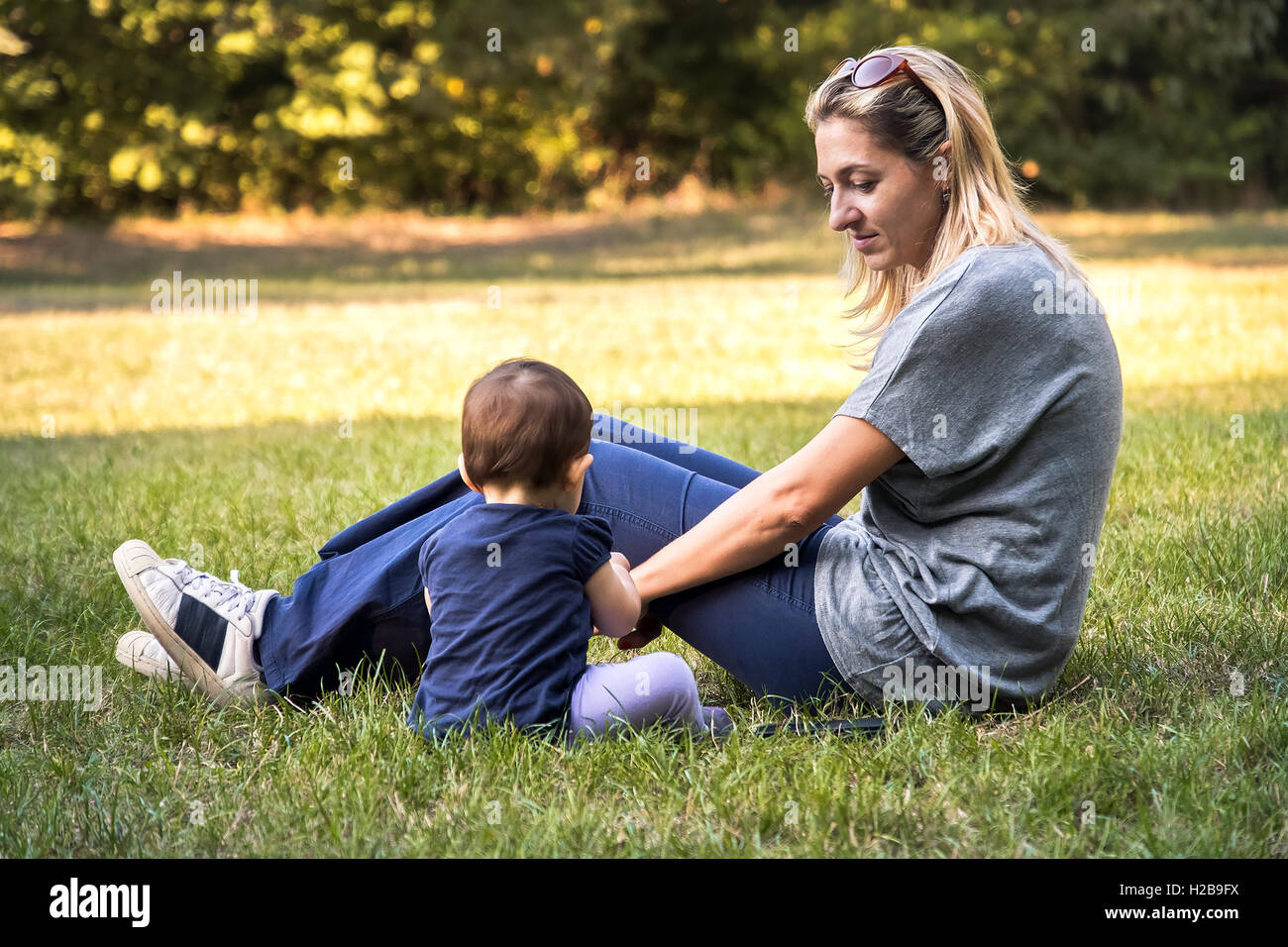 Une mère et son bébé nouveau-né fils assis dans l'herbe au parc passer du temps en famille dans un jardin Banque D'Images