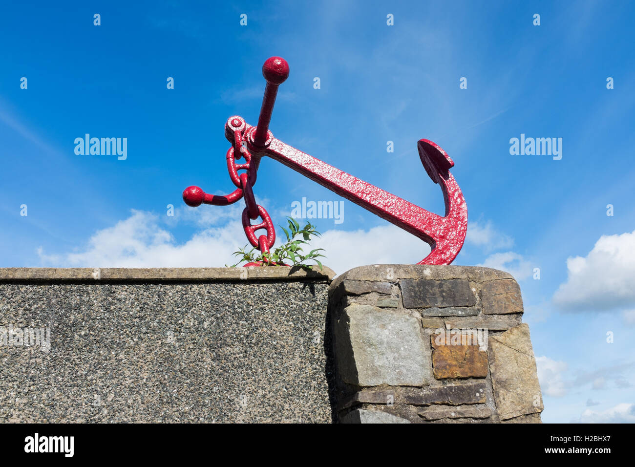 Old anchor peints en rouge assis sur un mur Banque D'Images