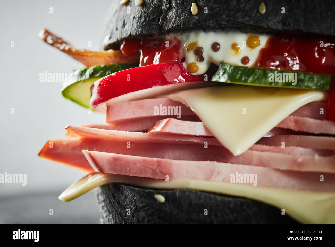 Burger au jambon et pain noir, avec de la laitue et de la mayonnaise et du ketchup sur fond blanc. Macro Banque D'Images