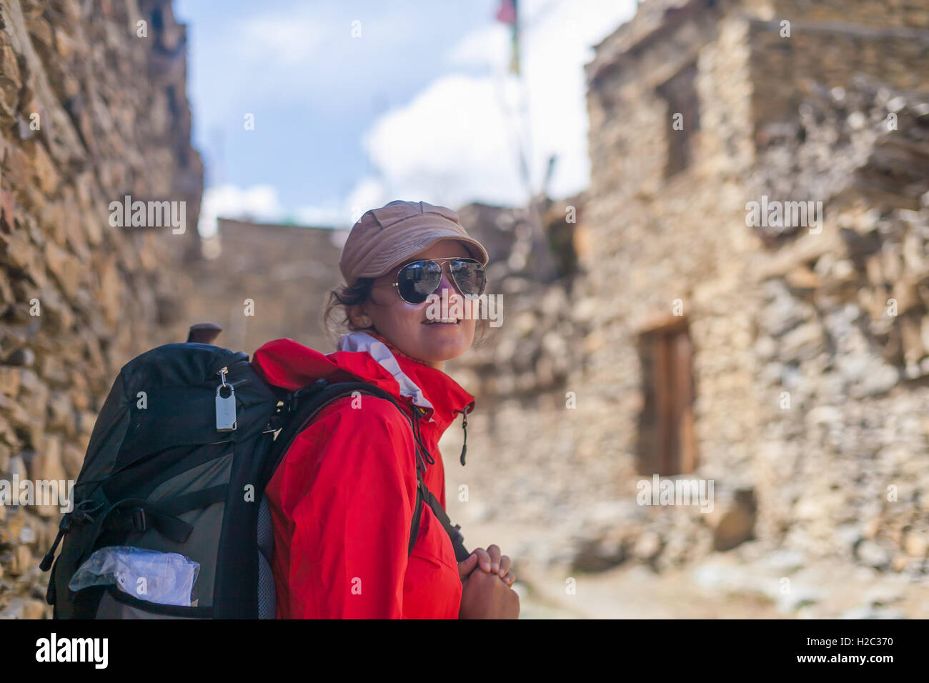 Portrait Young Woman Wearing Red Jacket Sac à dos Crossing Village Montagnes.Randonnée en montagne Sentier des roches.Vieille Ville Background Banque D'Images