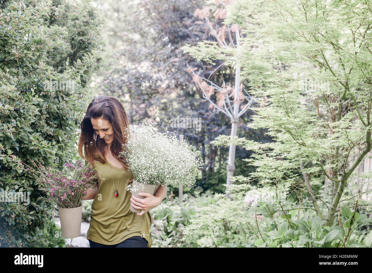 Femme marche à travers un jardin, portant un gros bouquet de fleurs. Banque D'Images