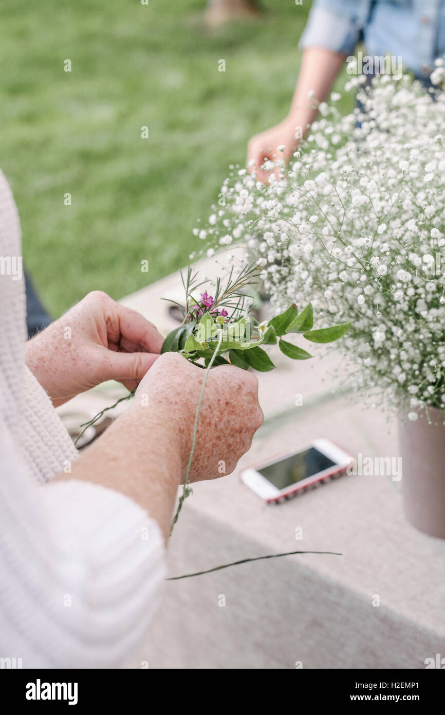 Portrait d'une femme, debout dans un jardin, faire une couronne de fleurs. Banque D'Images