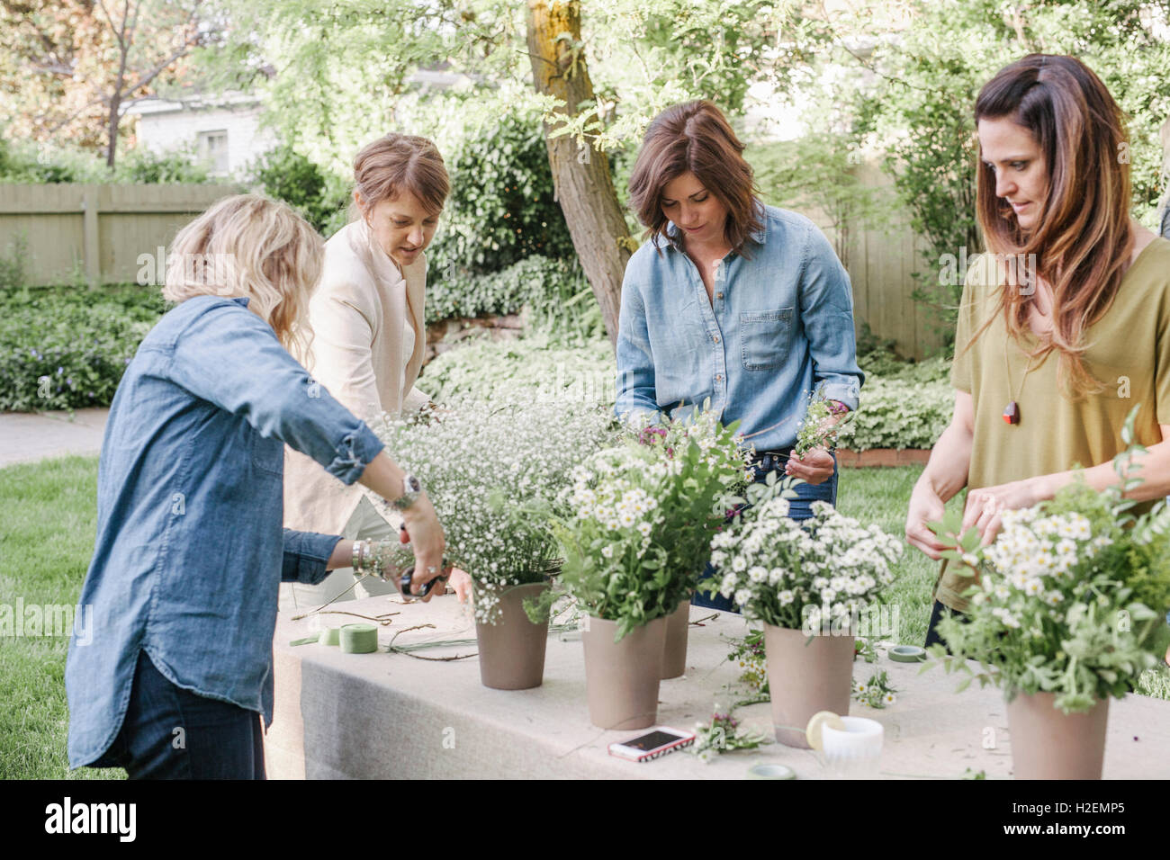 Quatre femmes, debout à une table dans un jardin de fleurs, des couronnes. Banque D'Images