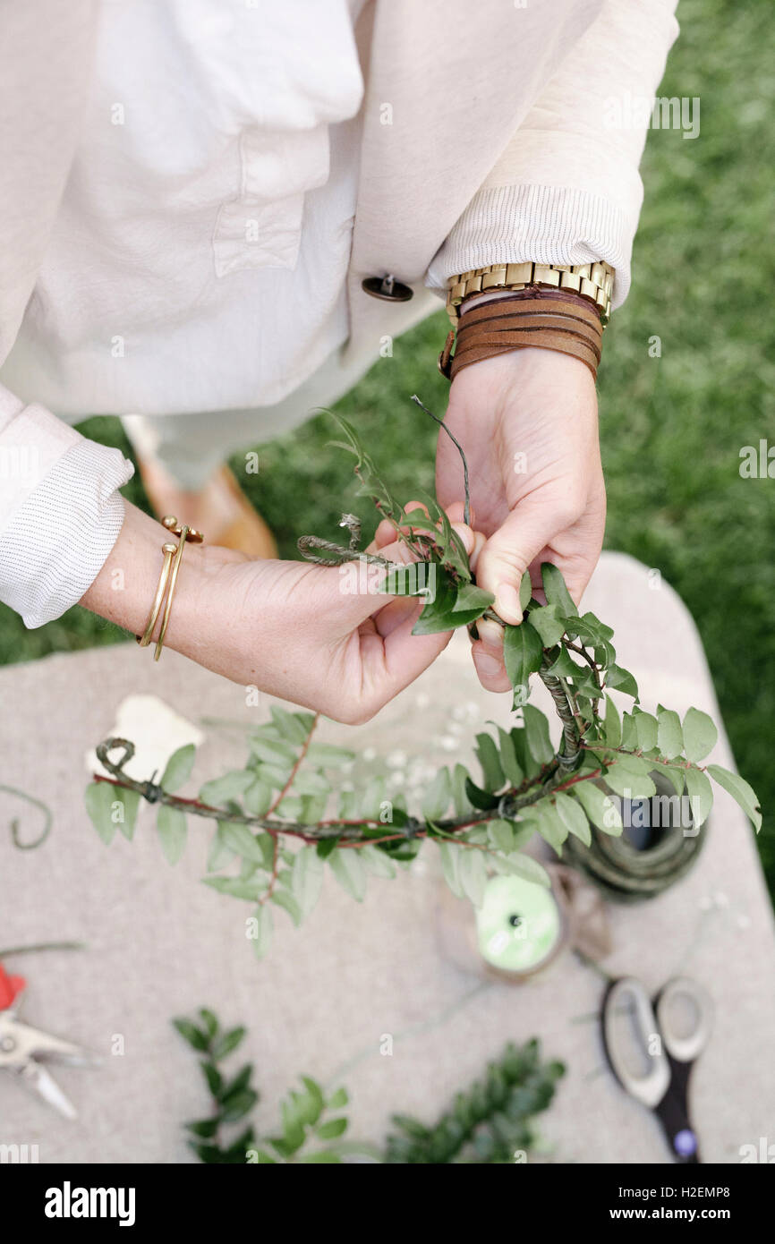 Portrait d'une femme, debout dans un jardin, faire une couronne de fleurs. Banque D'Images