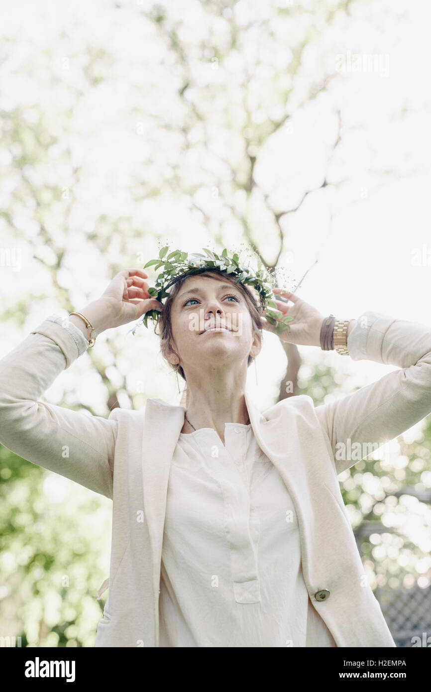 Femme debout dans un jardin, mettre une couronne de fleurs dans les cheveux. Banque D'Images