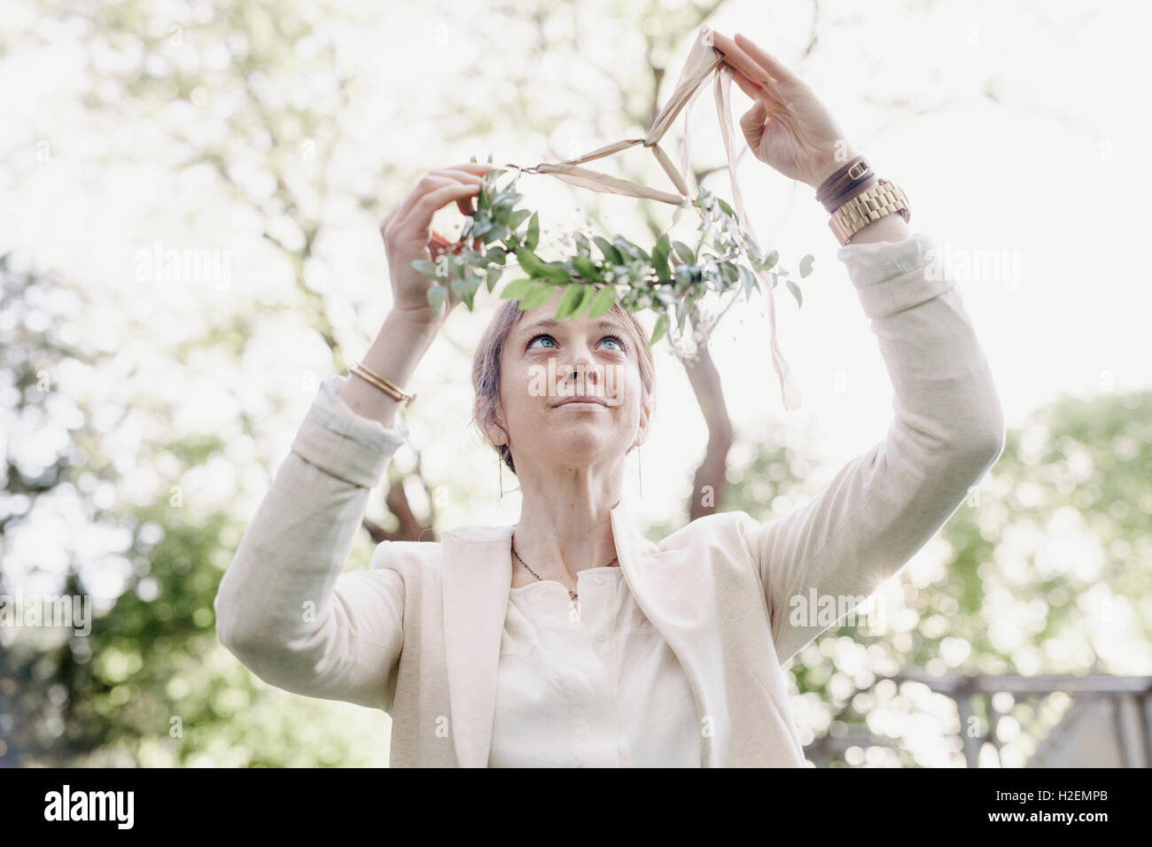 Femme debout dans un jardin, mettre une couronne de fleurs dans les cheveux. Banque D'Images