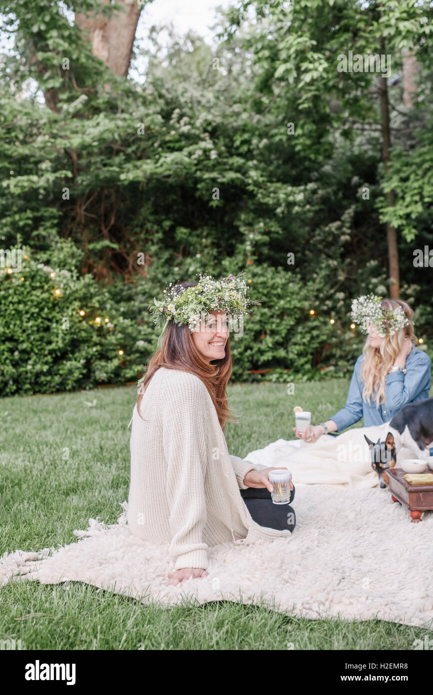 Deux femmes avec un sourire des couronnes de fleurs dans leurs cheveux assis dans un jardin. Banque D'Images