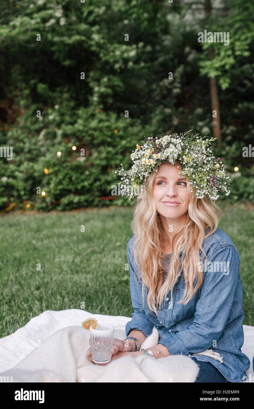 Femme souriante avec une couronne de fleurs dans les cheveux assis dans un jardin. Banque D'Images