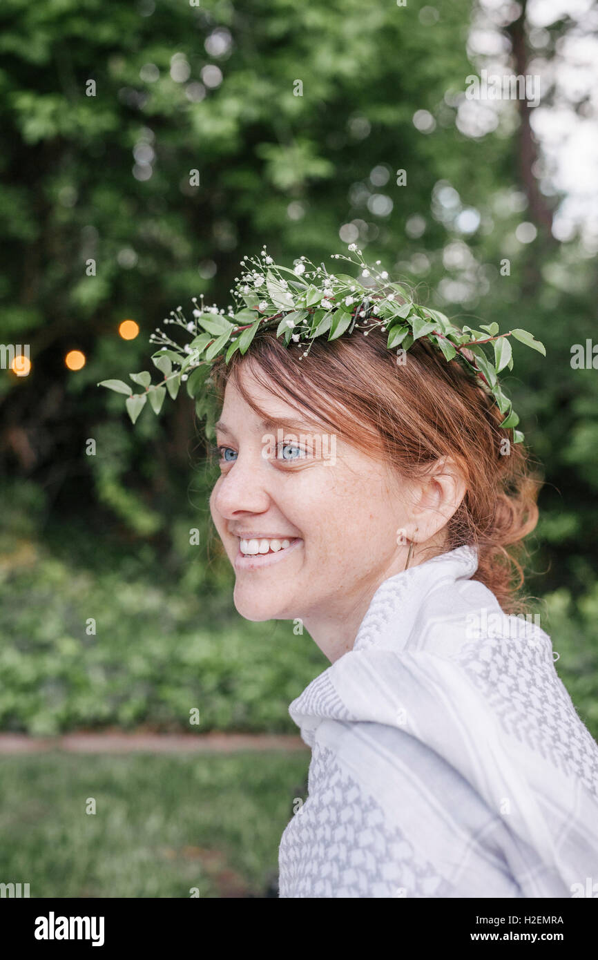 Femme souriante avec une couronne de fleurs dans les cheveux assis dans un jardin. Banque D'Images