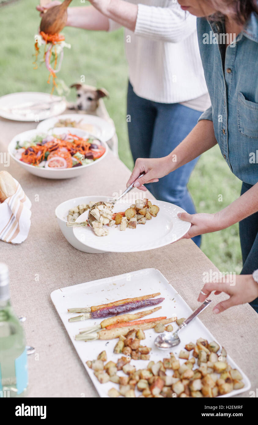 Les femmes avec couronne de fleurs dans leurs cheveux à un garden party, choisissent des aliments au buffet. Banque D'Images