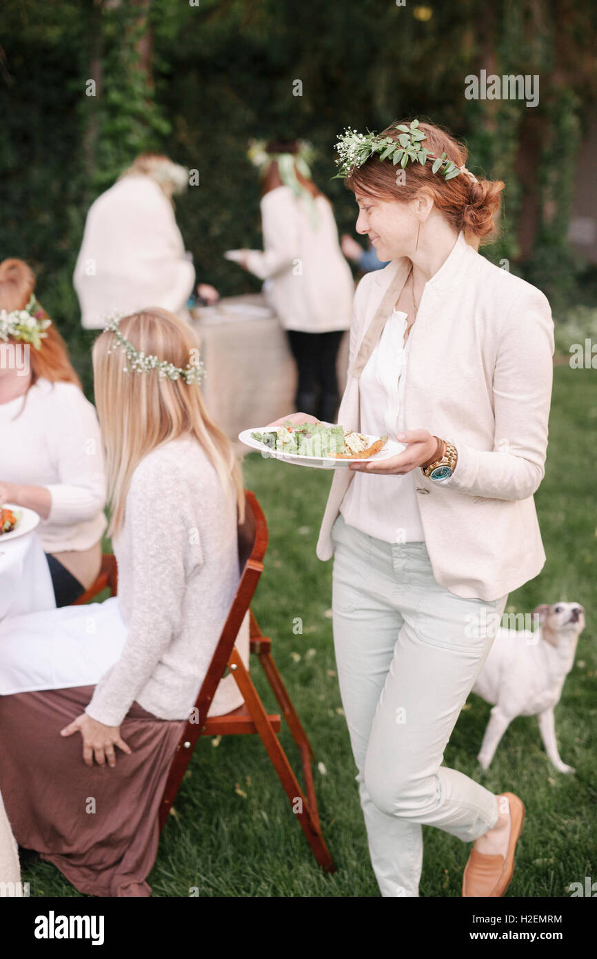 Groupe d'amis féminins avec des guirlandes de fleurs dans leurs cheveux, réunis autour d'une table dans un jardin. Banque D'Images