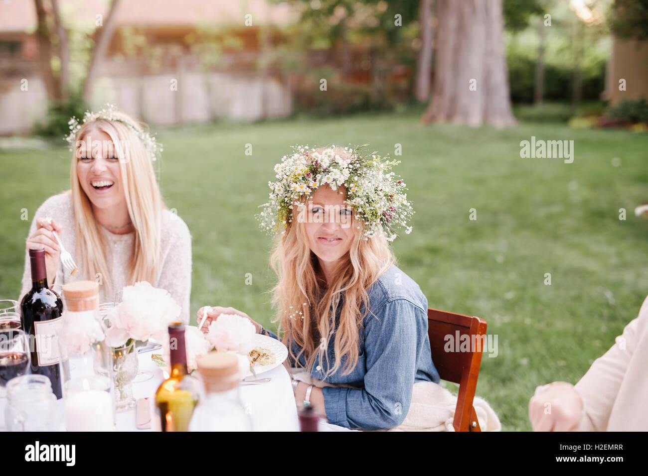 Deux femmes avec des couronnes de fleurs souriant dans leurs cheveux, assis à une table dans un jardin. Banque D'Images