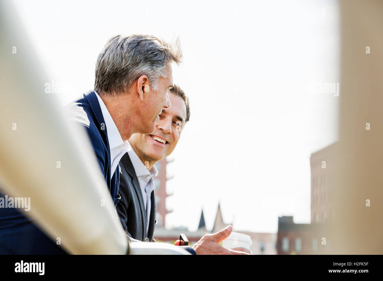 Deux personnes, les hommes parlent ensemble en plein air s'appuyant sur une balustrade, en prenant une pause-café. Banque D'Images