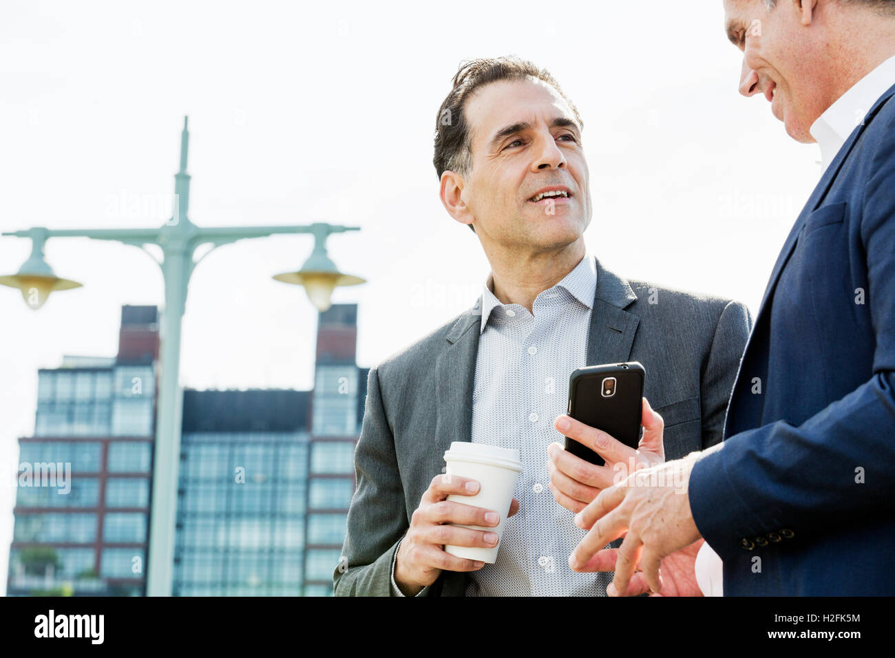 Deux personnes, les hommes parlent ensemble en plein air s'appuyant sur une balustrade, en prenant une pause-café. Banque D'Images