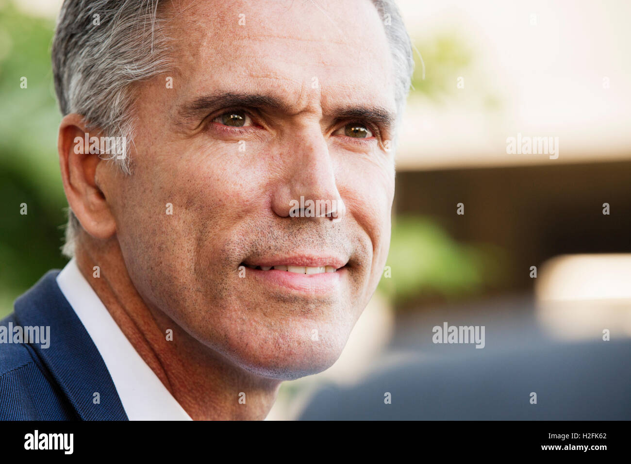 Un homme en chemise blanche avec des cheveux gris, souriant, la tête tournée à parler à une autre personne . Banque D'Images