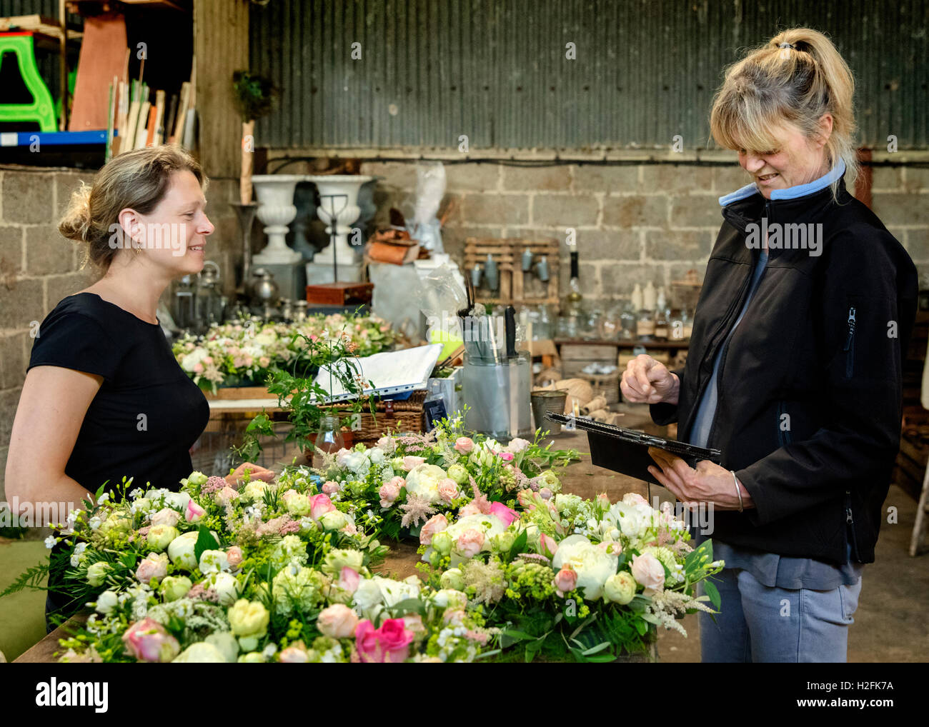 Deux femmes, l'un à l'aide d'une tablette numérique. Fleuristes à un établi décoration de table, des arrangements de fleurs roses et blanches. Banque D'Images