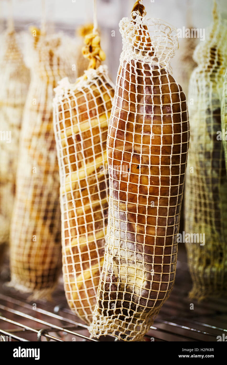 Close up de la viande séchée à l'air emballé dans des filets, suspendu dans une charcuterie. Banque D'Images