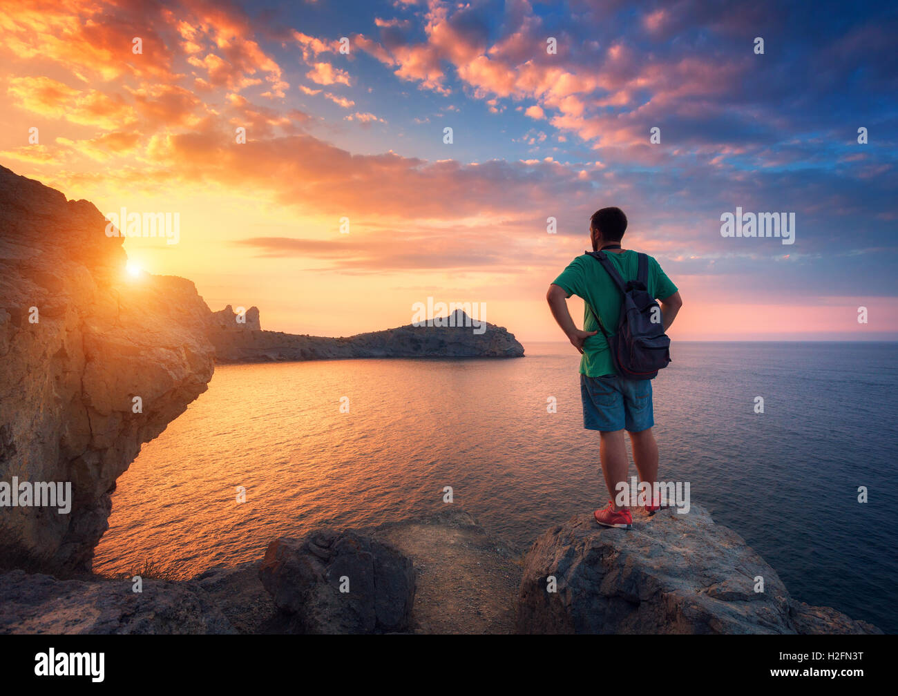 Beau paysage d'été avec l'homme debout avec sac à dos sur la pierre au bord de l'atlantique contre le ciel avec les nuages colorés au soleil Banque D'Images