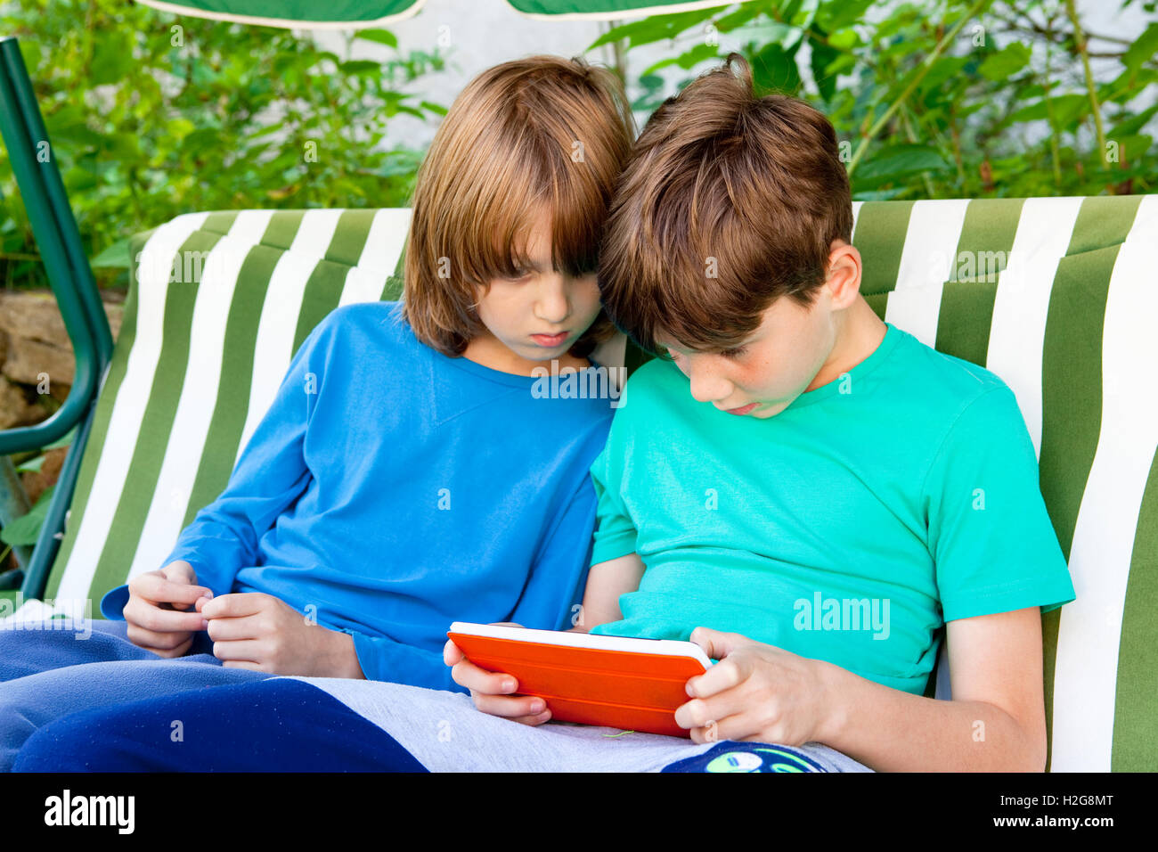 Deux garçons assis dans le jardin à jouer avec Tablet Banque D'Images