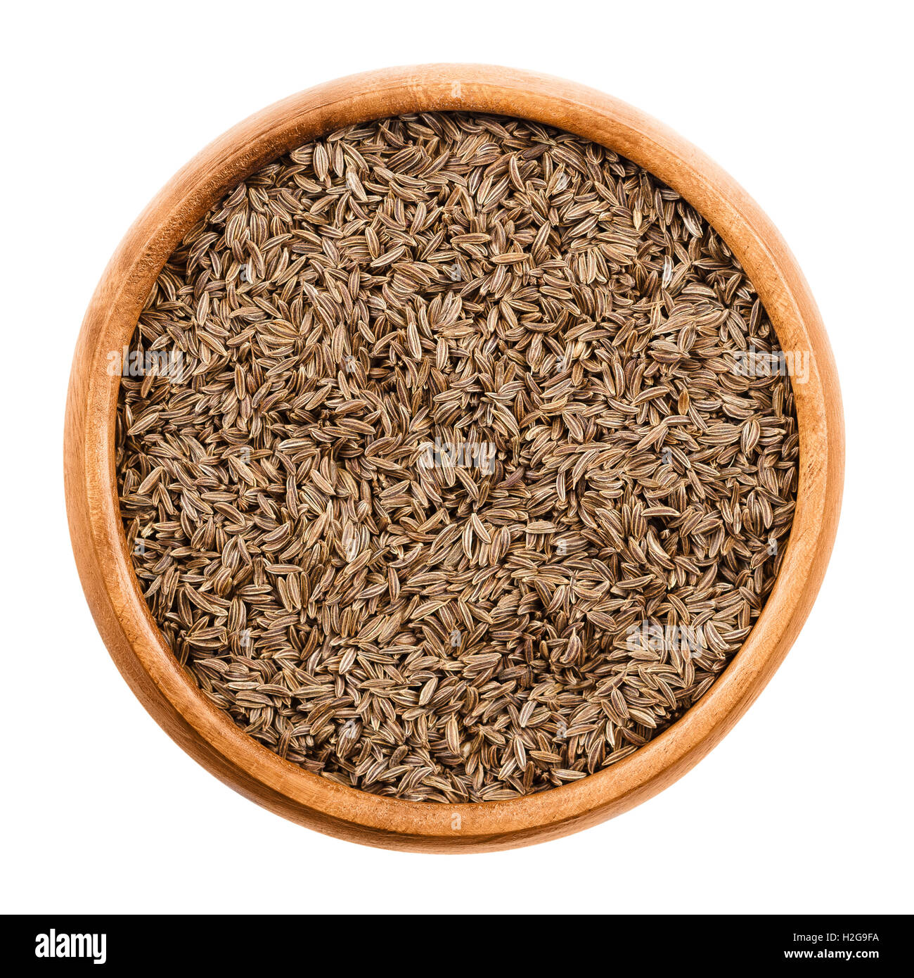 Graines de cumin dans bol en bois sur fond blanc. Les fruits entiers séchés de Persian, cumin Carum carvi, avec de l'anis comme saveur. Banque D'Images